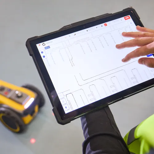 Opérateur avec une tablette pilotant le robot traceur jaune sur une dalle de béton