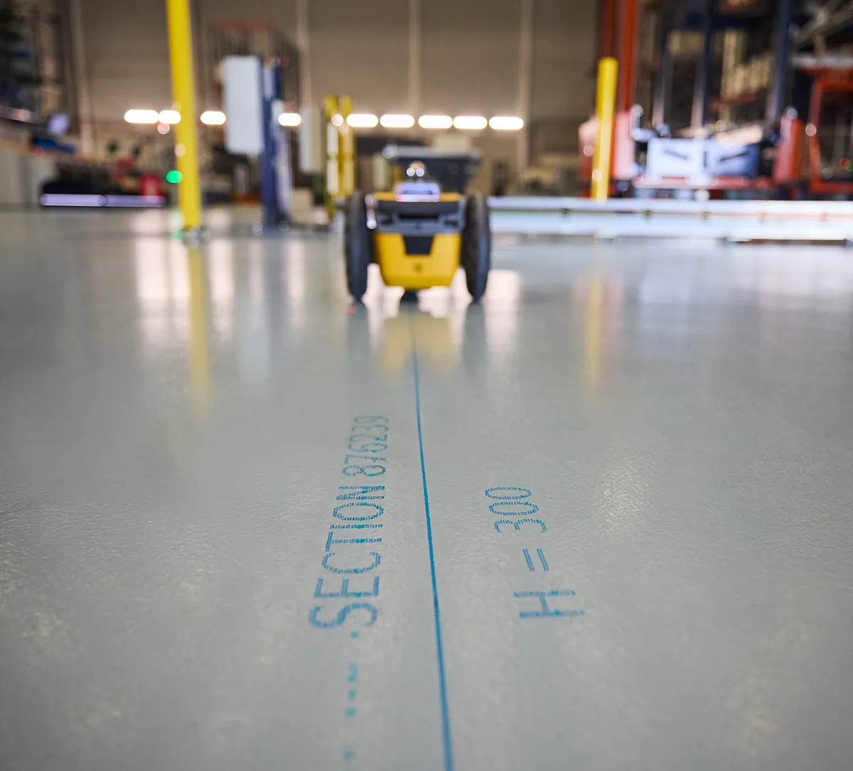 Robot traceur jaune imprimant des lignes de repérage sur une dalle de béton
